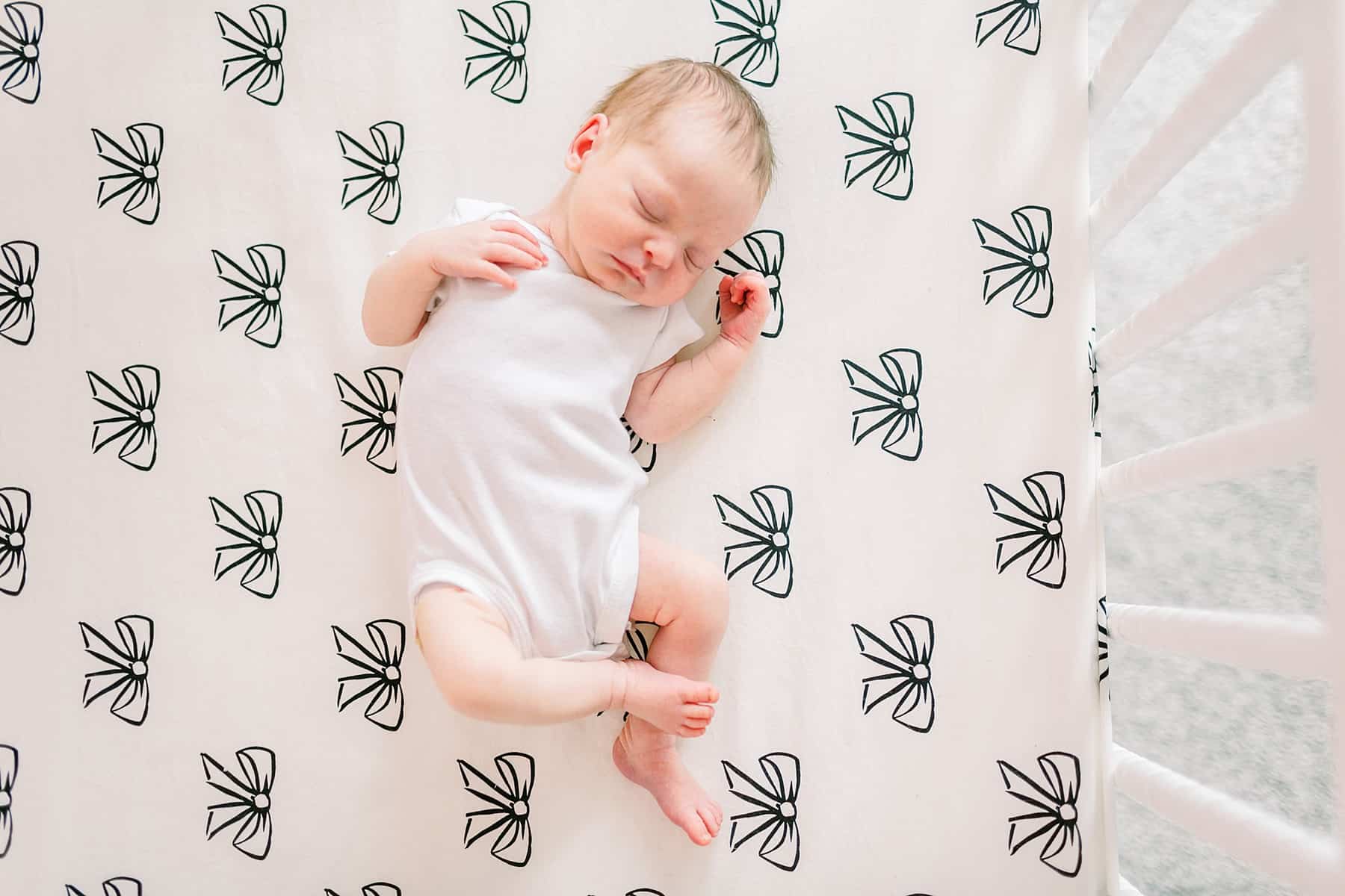 baby laying in crib wearing white onesie - newborn photography south florida