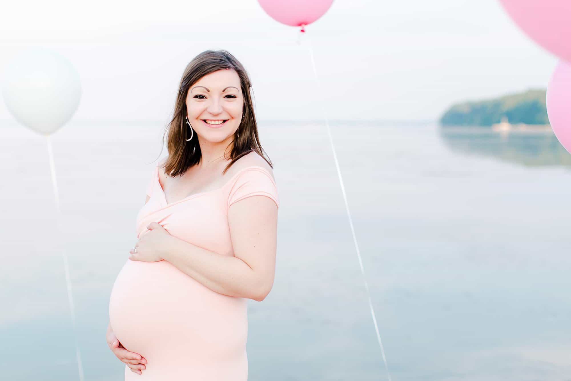 pregnant woman in tight peachy pink dress surrounded by pink and white balloons - What to Wear for Beach Maternity Photos | Maternity Photographer Miami
