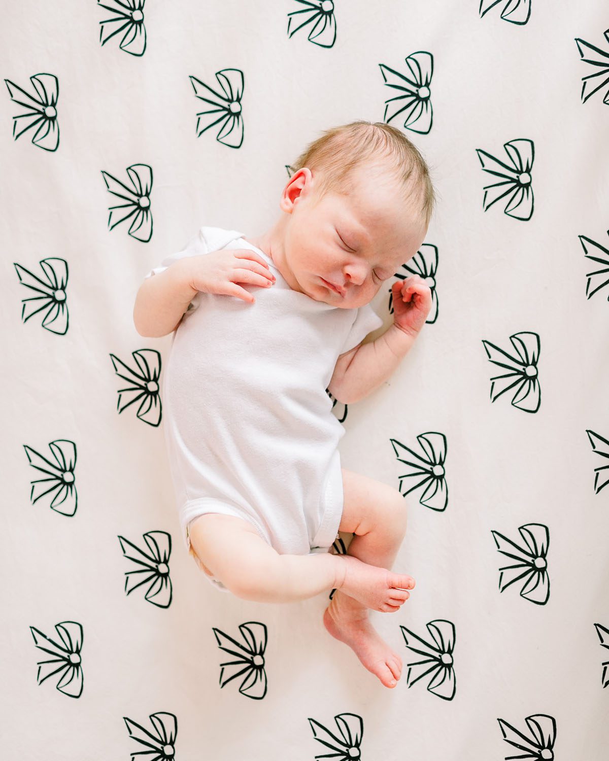 baby sleeping in white onesie on black bow crib sheet by Miami Newborn Photographer