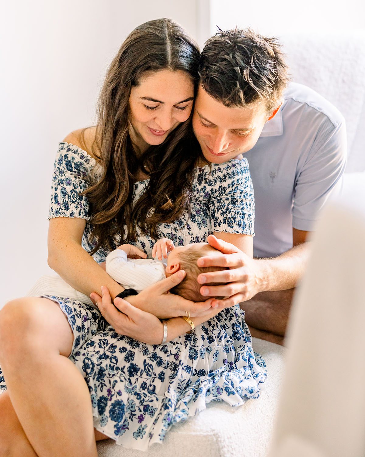 Parents cuddling baby sitting on chair by Miami Newborn Photographer