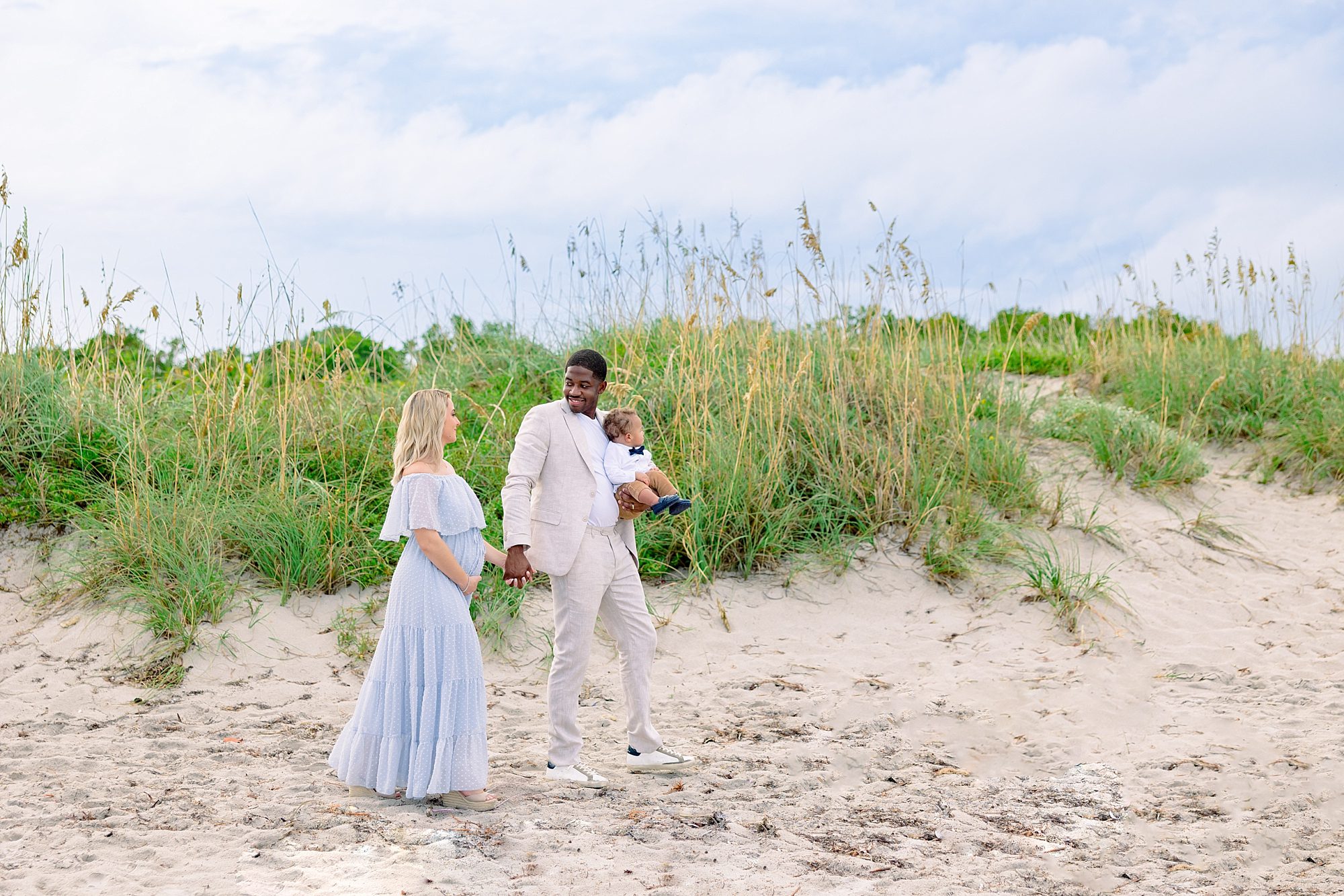 mom in off the shoulder light blue dress walking holding hands with husband in linen suit at a miami maternity photography session