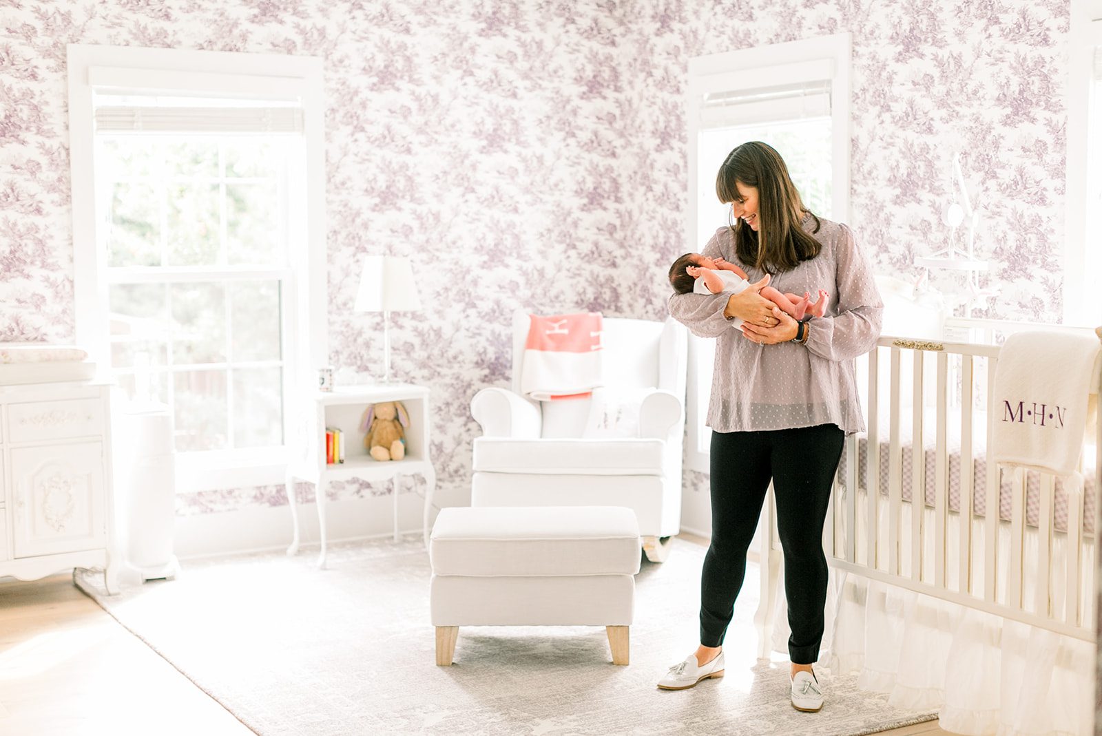 Mother gently holding her newborn baby while standing in a softly lit nursery at home