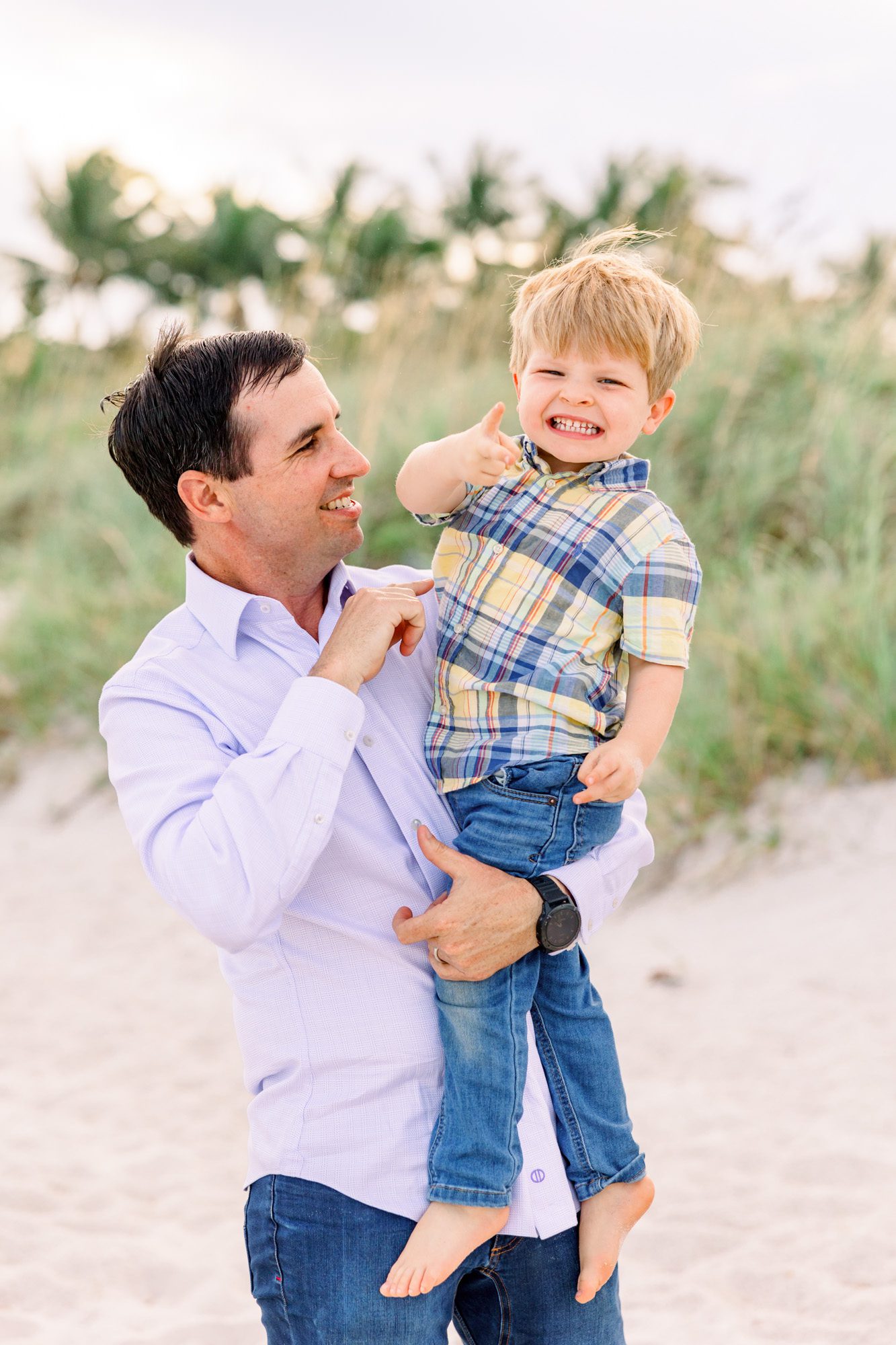 Boy giving thumbs-up and smiling at camera while Dad holds him