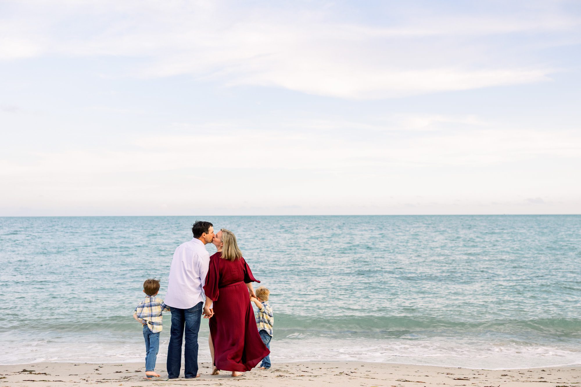 Parents kissing on Florida beach while holding young sons' hands