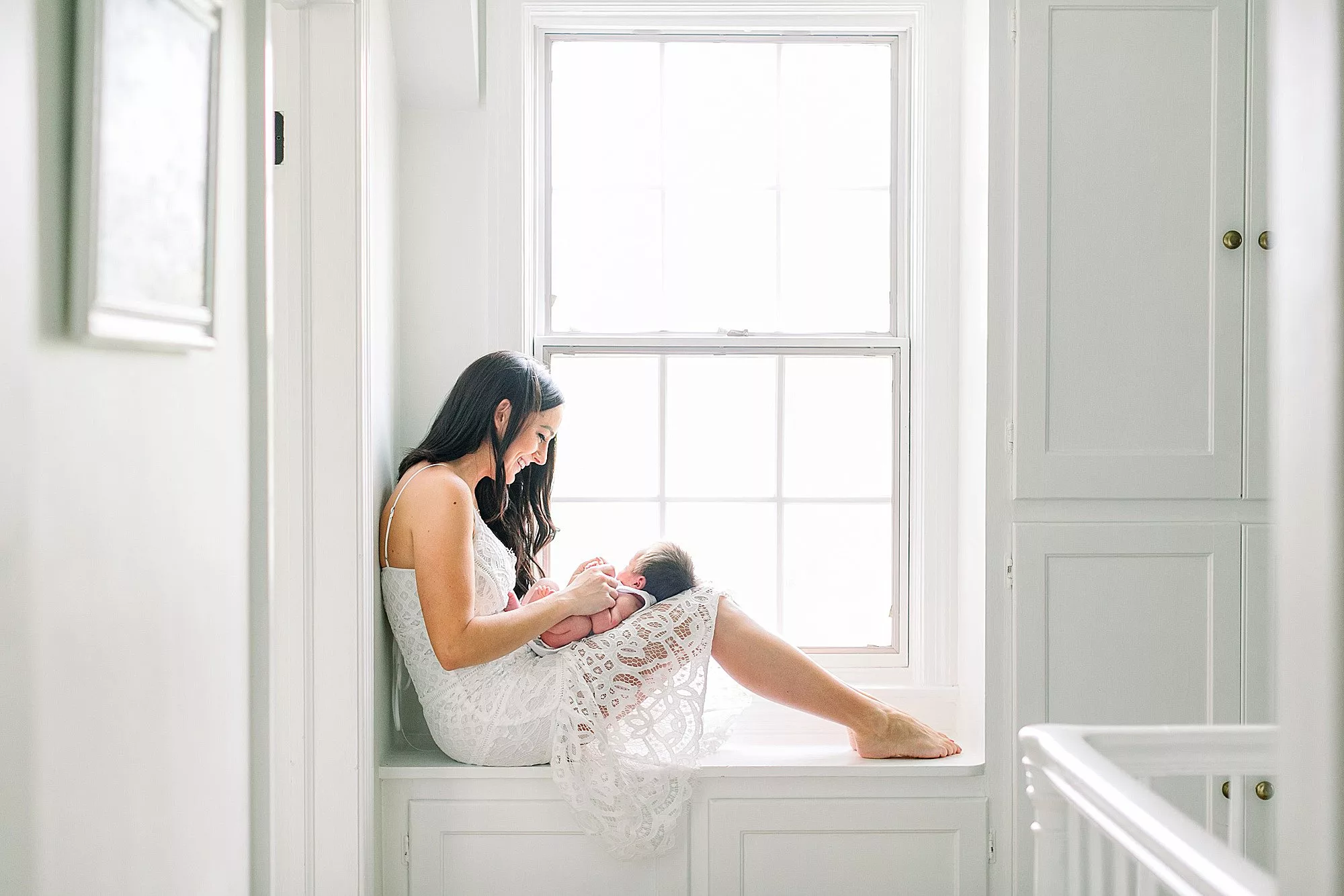 Mom in white dress in white hallway cuddling baby in her lap for Cville Birth Center article