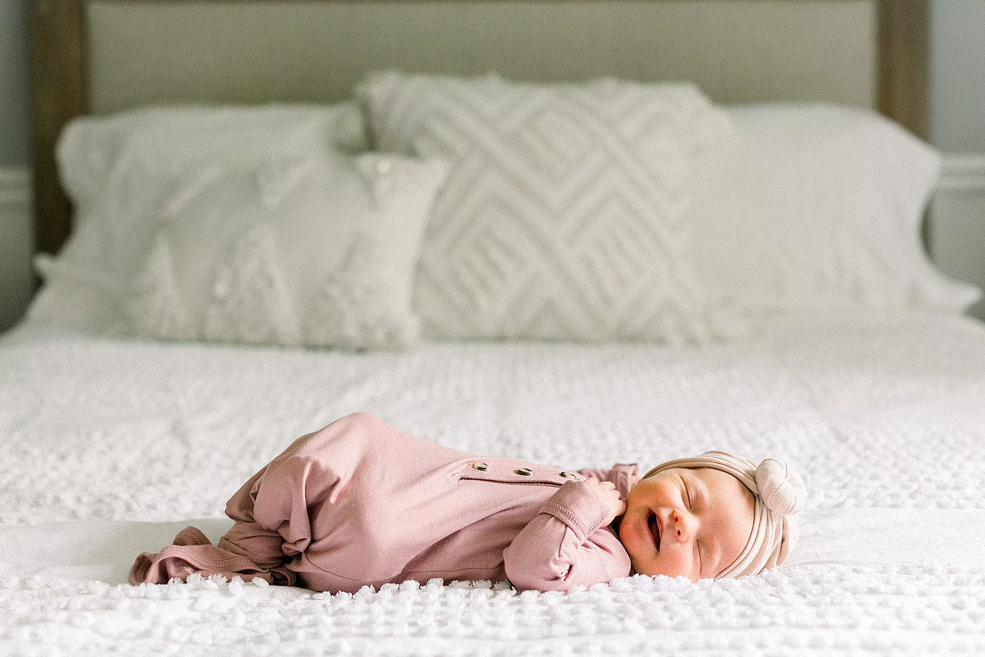 Smiling baby sleeping on bed in pink gown