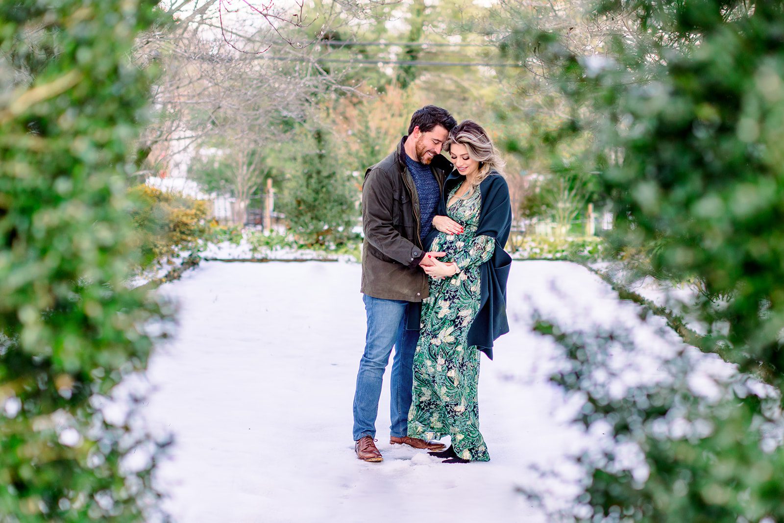 How a Richmond VA Fertility Clinic Can Help Your Pregnancy! 1 husband and wife stand in a winter garden holding and looking at her pregnant belly a Richmond VA Fertility clinic can help you