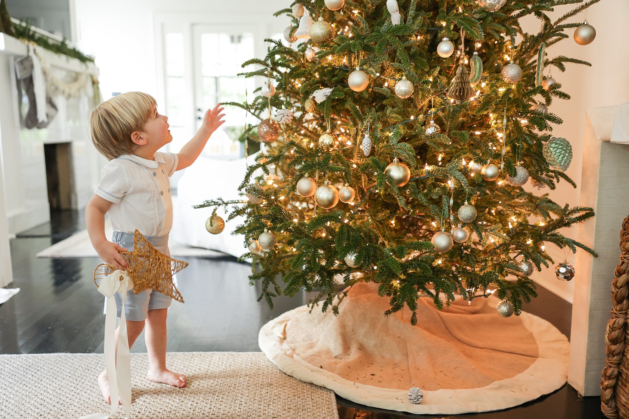 little boy in smocked outfit holding star next to christmas tree
