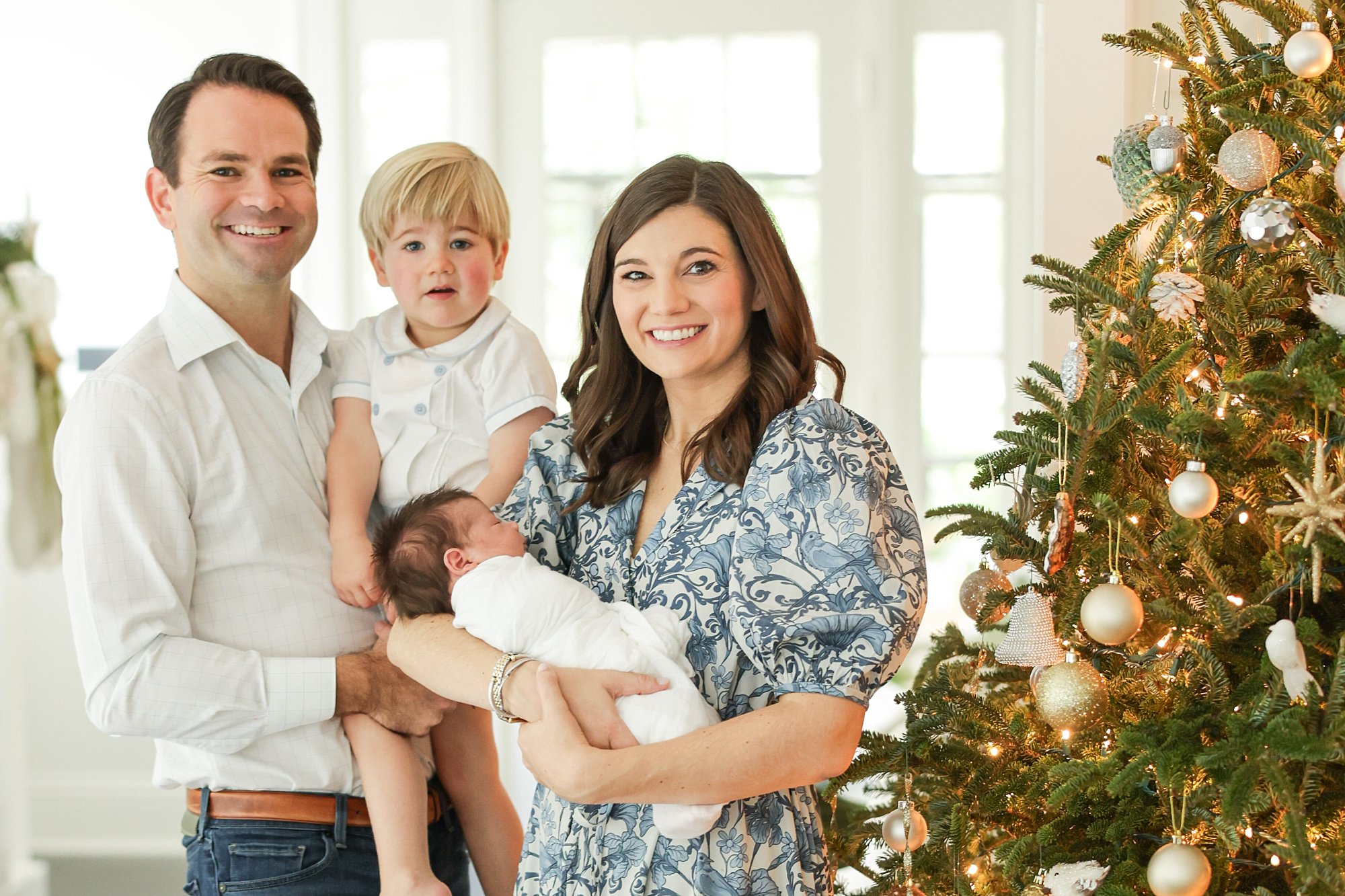 Family of 4 posing by Christmas tree for family holiday photos