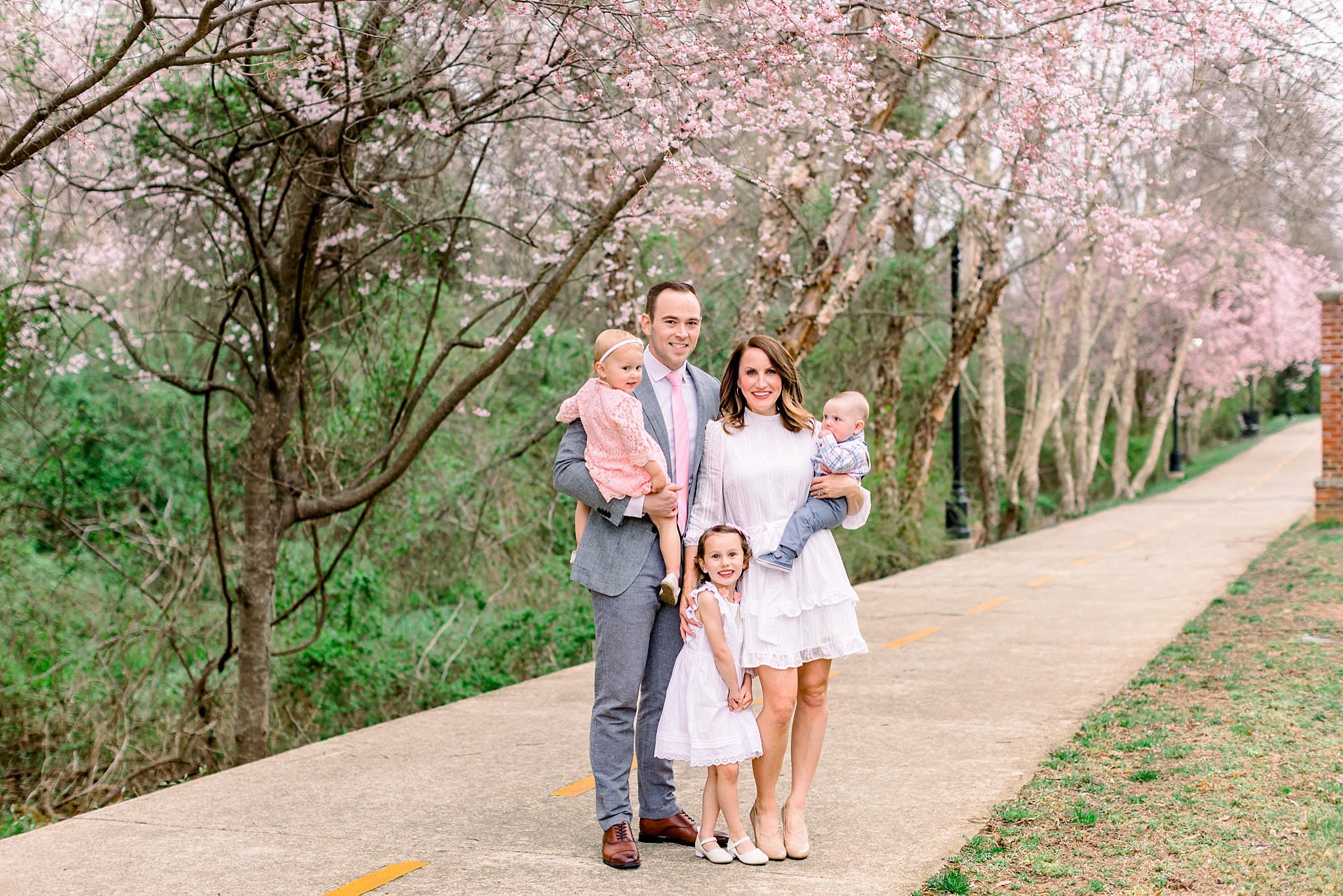 Spring Family Photo Outfits: A Complete Style Guide 12 Family of four in coordinated spring family photo outfits walking through a cherry blossom path with light blues and pinks
