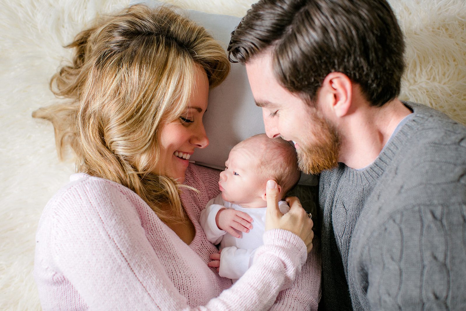 The Best Richmond Midwives : 6 Teams to Guide You Through Birth 8 Mom and dad lying on their bed with their newborn baby resting between them, both parents gazing lovingly down at their child