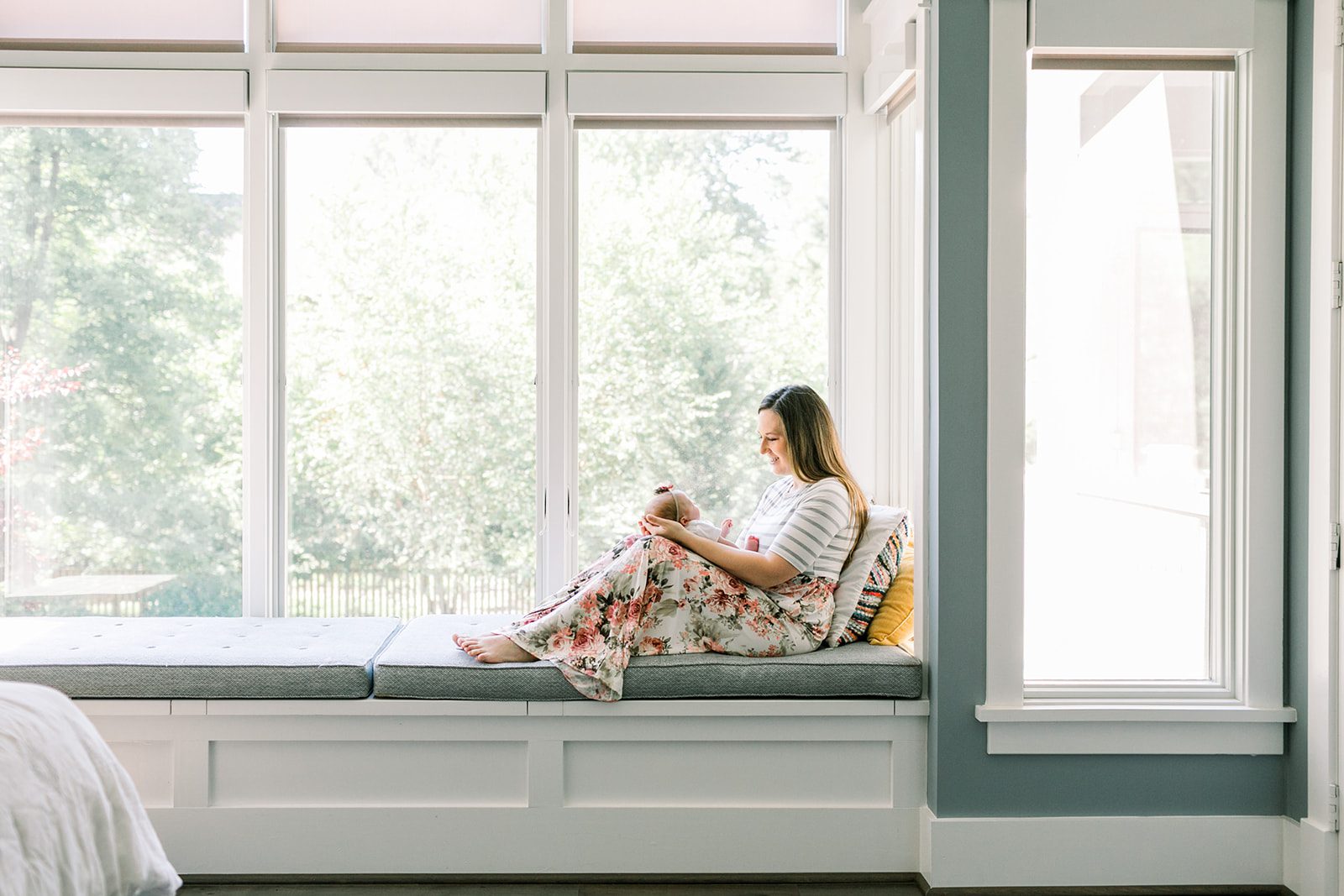The Best Richmond Midwives : 6 Teams to Guide You Through Birth 5 Mother sitting on a large window bench, gently holding her newborn on her lap, bathed in natural light and sharing a peaceful moment together after using Richmond midwives for her birth.