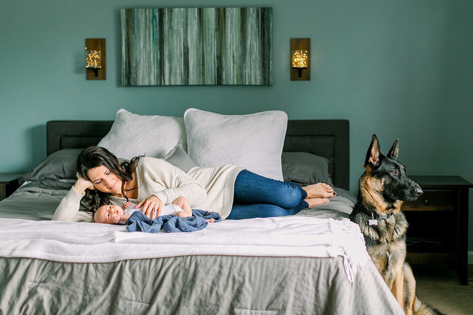 Why Motherhood Photography is So Important 9 A mom laying on her bed with her newborn baby nestled beside her, while the family dog lies close by, keeping a watchful and protective gaze over the peaceful moment.