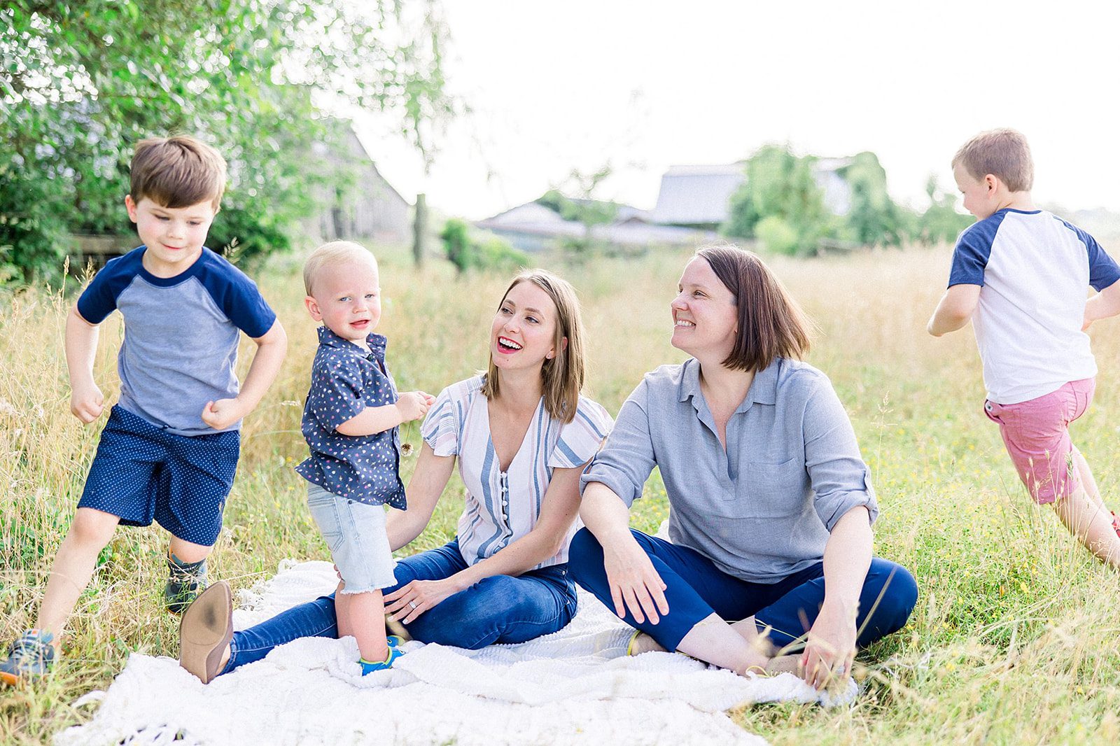 Why Motherhood Photography is So Important 6 Two moms surrounded by their children running joyfully around them in a field, captured in a lively, playful moment by Melissa Arlena Photography, with the family enjoying the freedom and fun of the outdoors